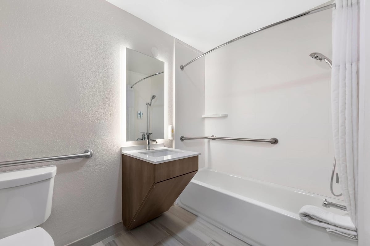 A modern bathroom with a toilet, sink, mirror, shower, and grab bars.
