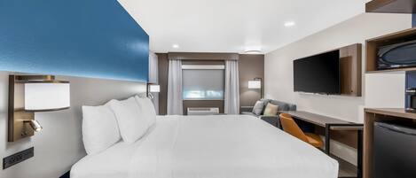A hotel room with a bed, desk, TV, and a minibar.
