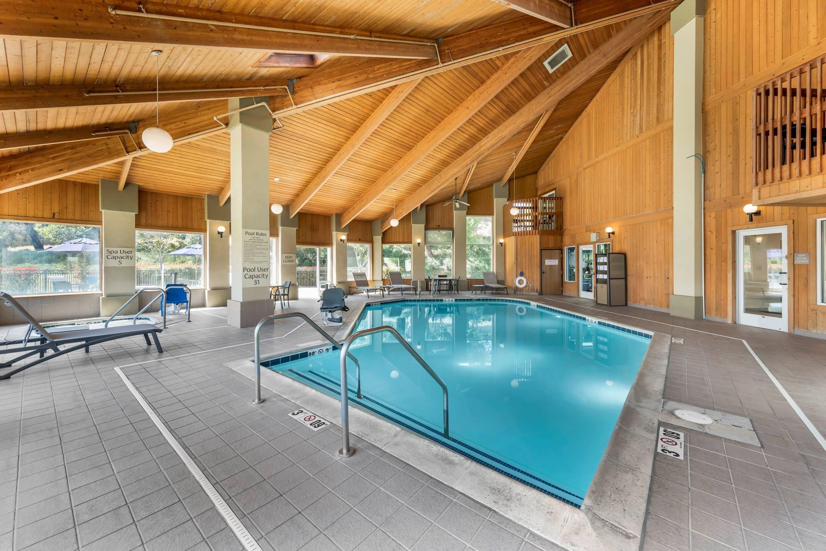 An indoor swimming pool with wooden beams, tiled flooring, and lounge chairs.