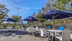 An outdoor patio area with tables and chairs, shaded by large umbrellas, and surrounded by a fence. - Comfort Inn Fontana (Fontana)
