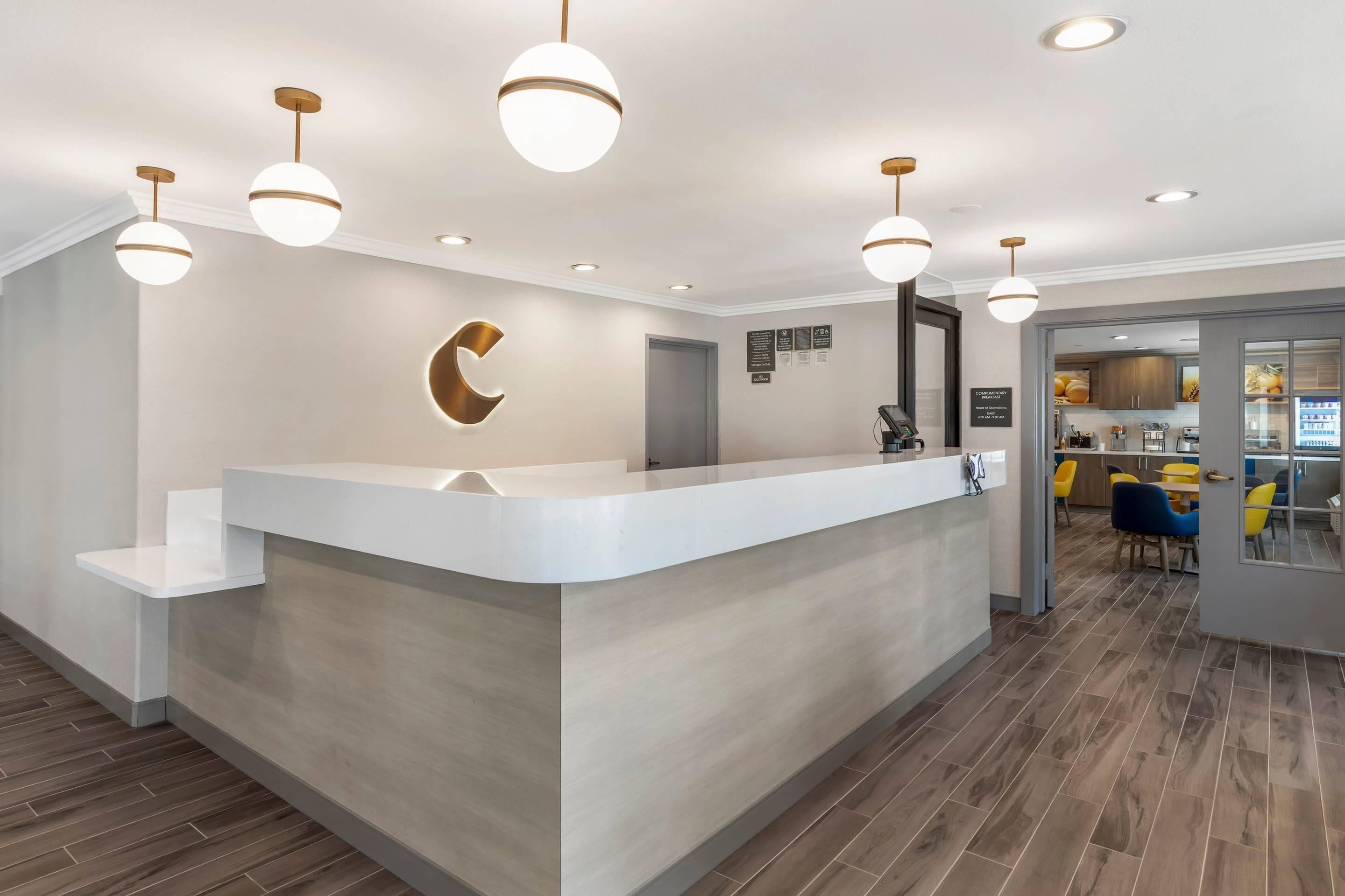A reception desk with a modern design, a circular logo on the wall, and a view into the dining area with yellow chairs.