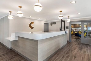 A reception desk with a modern design, a circular logo on the wall, and a view into the dining area with yellow chairs. - Comfort Inn Fontana (Fontana)