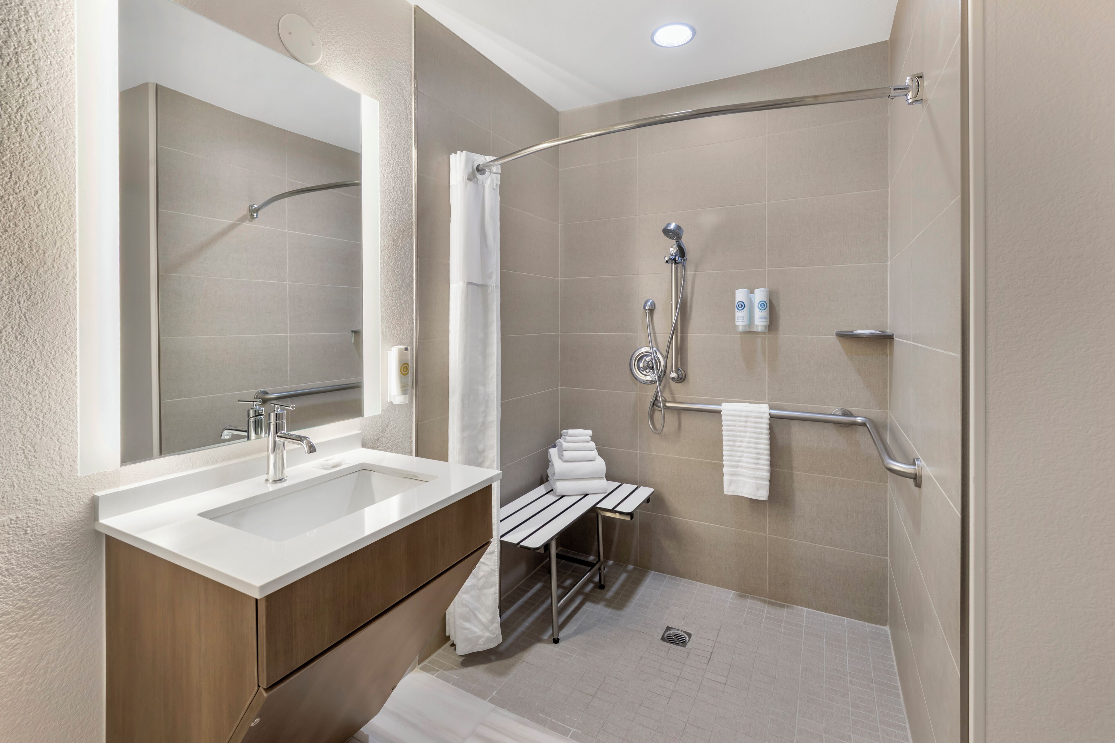 A modern bathroom with a double sink, a shower with a handheld showerhead, and a grab bar.