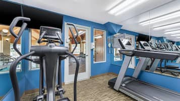 Un gimnasio con cintas de correr, elíptica y un espejo grande.
