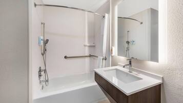 A modern bathroom with a bathtub, a shower, a vanity with a mirror, and a towel rack.
