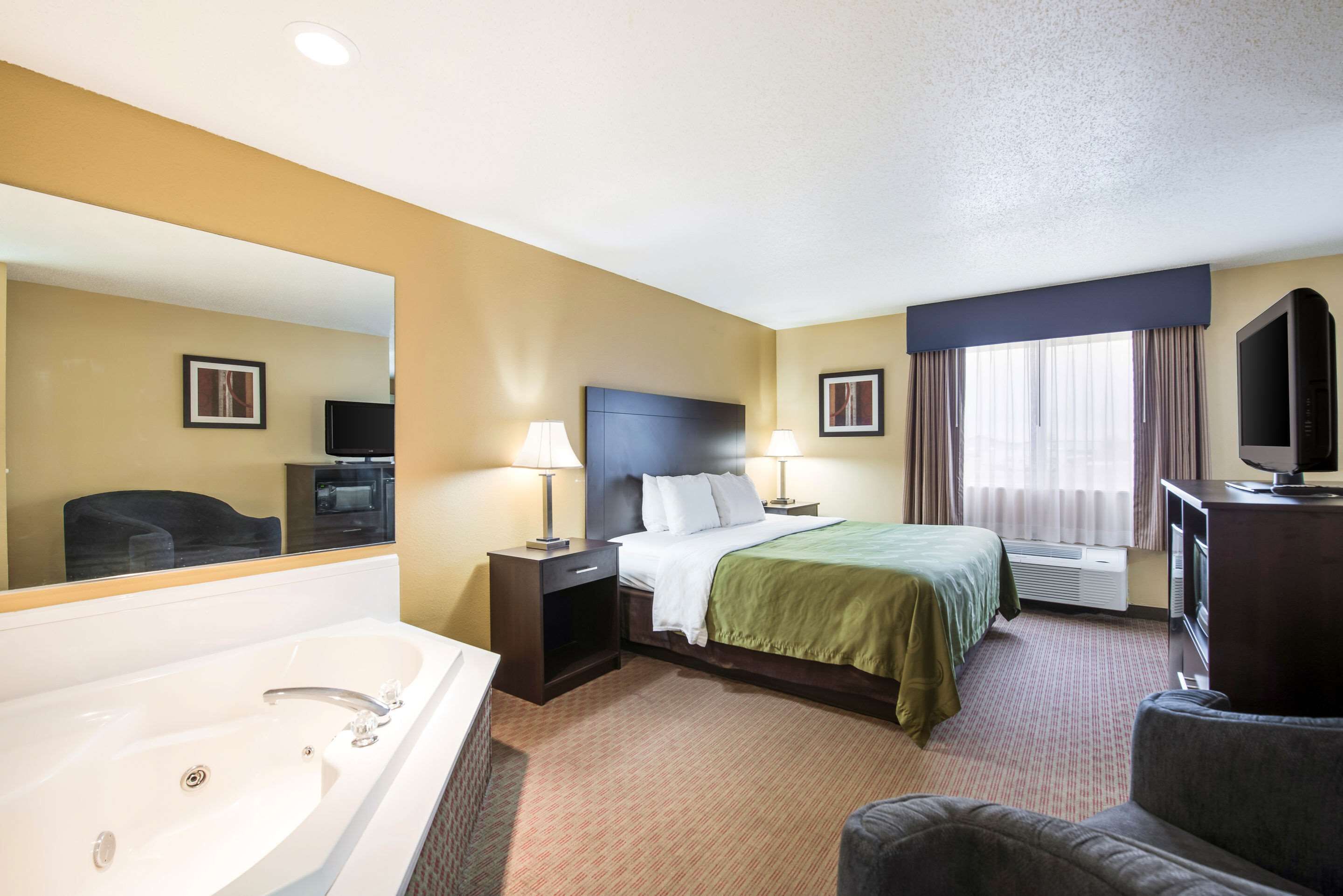 Een hotelkamer met een groot bed, een zithoek met een fauteuil, een televisie, een bureau en een badkamer met bad en wastafel.