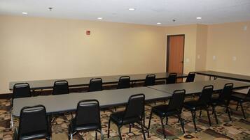 Una sala de conferencias con una larga mesa y numerosas sillas, paredes color beige y alfombra estampada.