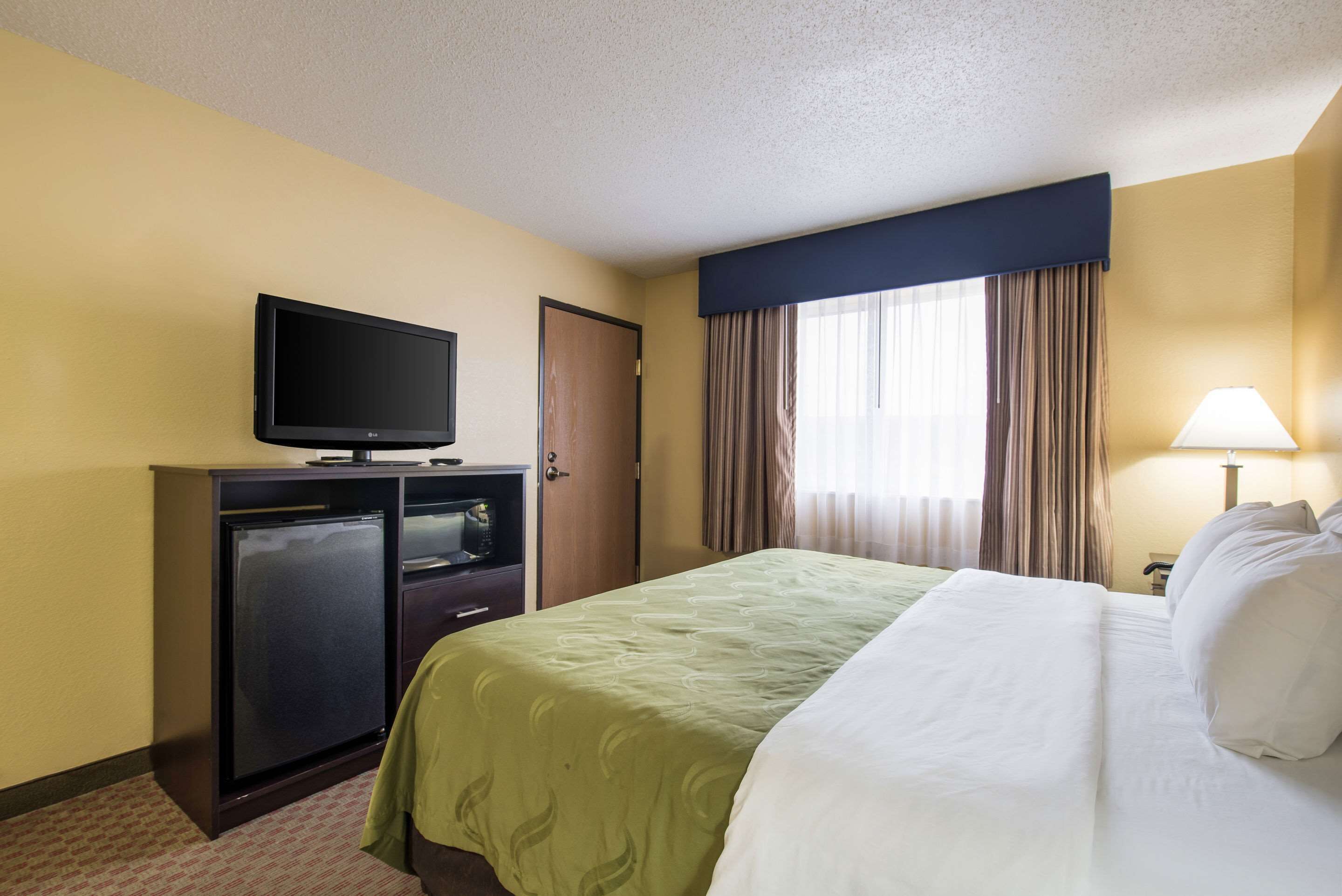 Een hotelkamer met een bed, een televisie op een kast, een bureau en een raam met gordijnen.