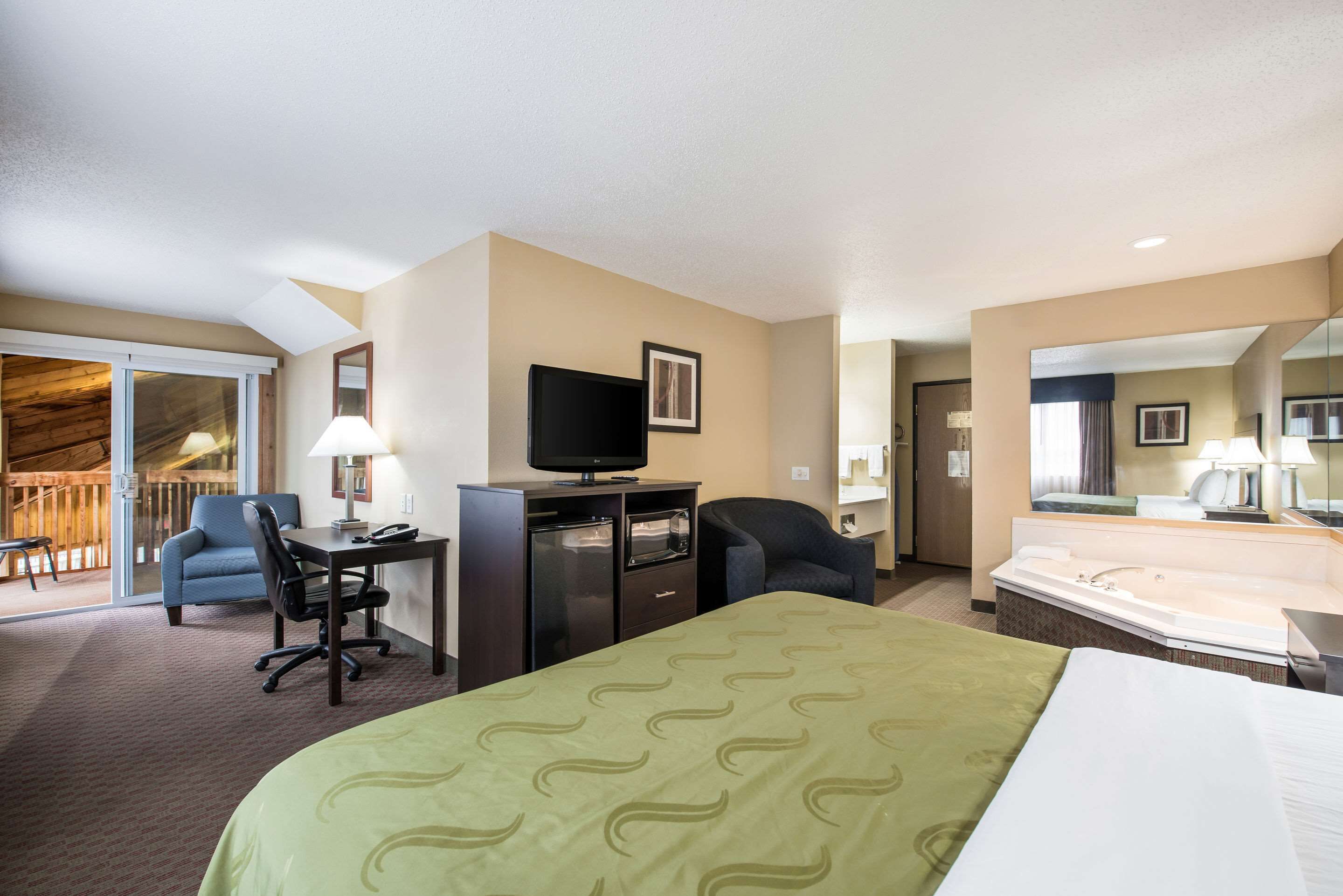 A hotel room with a bed, desk, chair, television, and a bathroom with a bathtub.