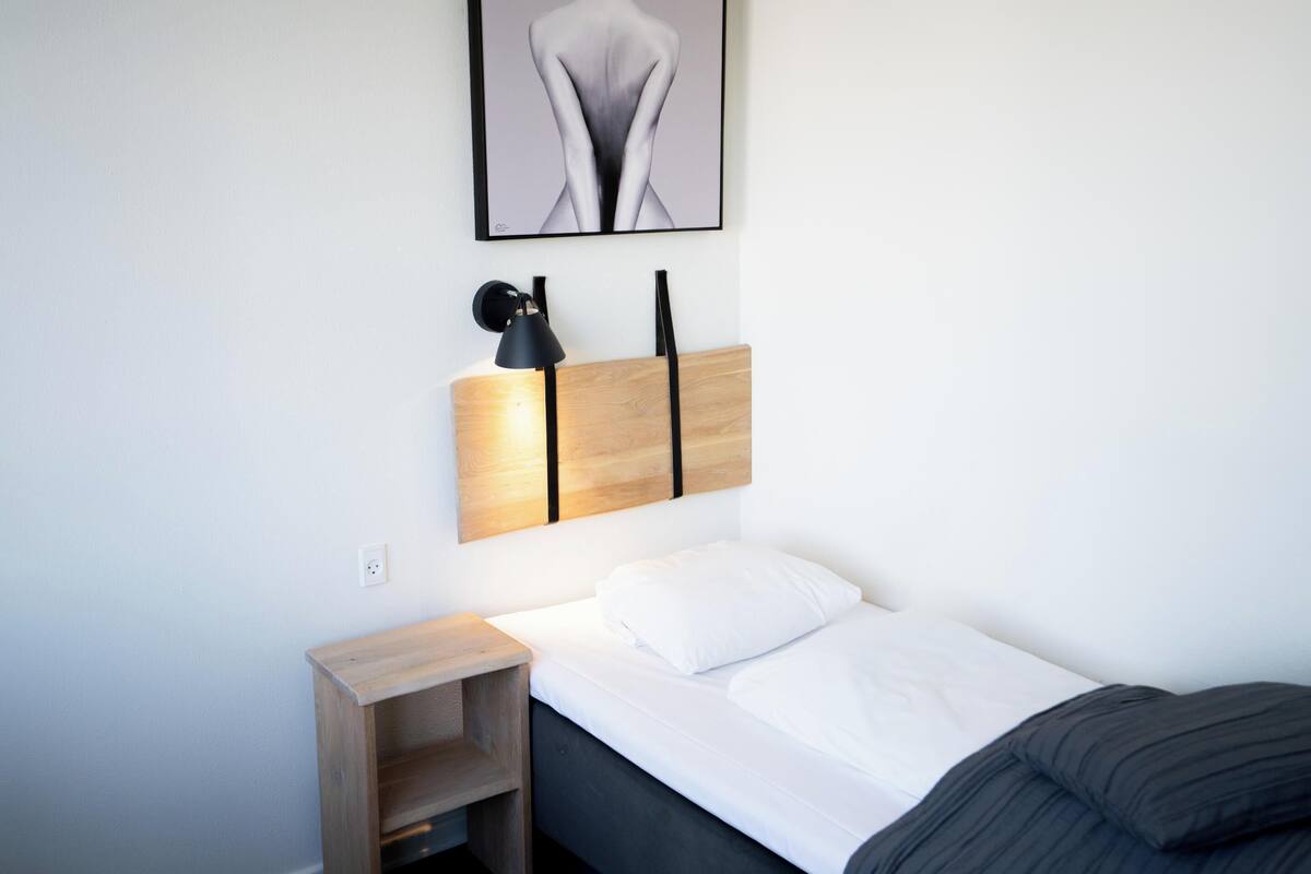 A neatly arranged bedroom with a bed, bedside table, and a wall-mounted lamp.