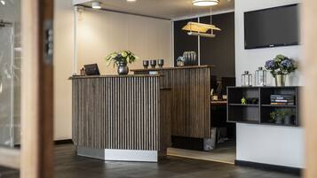 A reception area with a wooden reception desk, a potted plant, and a shelf with books and decorative items.