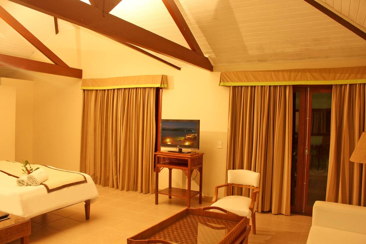 A hotel room with a bed, a desk with a TV, a chair, and a view of the outdoors through a window.