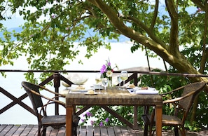 Un espace de restauration en plein air, avec des chaises en osier et une table dressée pour deux personnes, donnant sur une étendue d’eau.