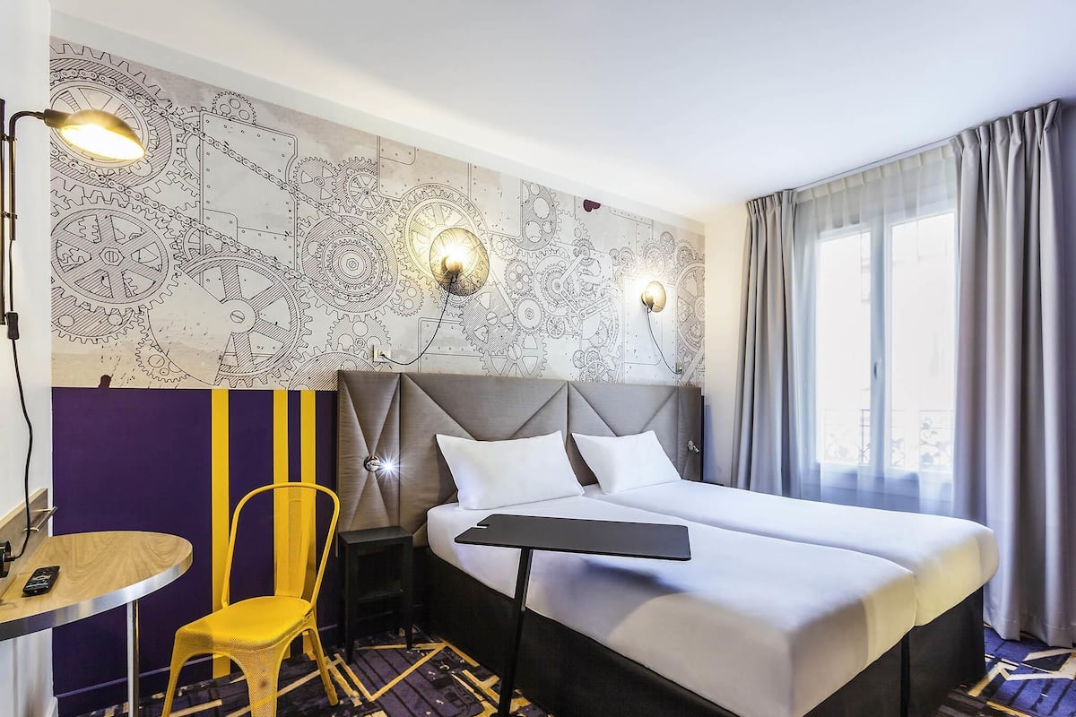Una habitación de hotel con una cama, un escritorio, una silla y una pared con diseño mecánico.
