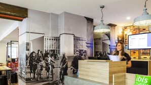 A reception desk with a large black and white photograph of people on bicycles, a wooden counter, and a green 'ibis Styles Hotels' sign. - Ibis Styles Paris Mairie de Clichy (Clichy)