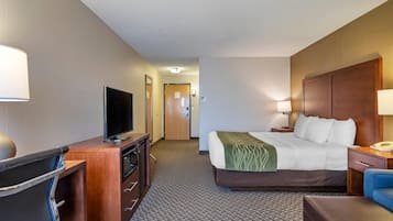 A hotel room with a bed, a desk with a television, a chair, a lamp, and a nightstand.