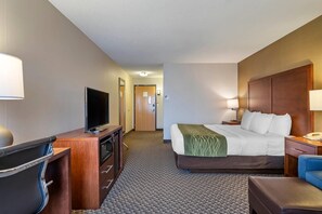 A hotel room with a bed, a desk with a television, a chair, a lamp, and a nightstand.