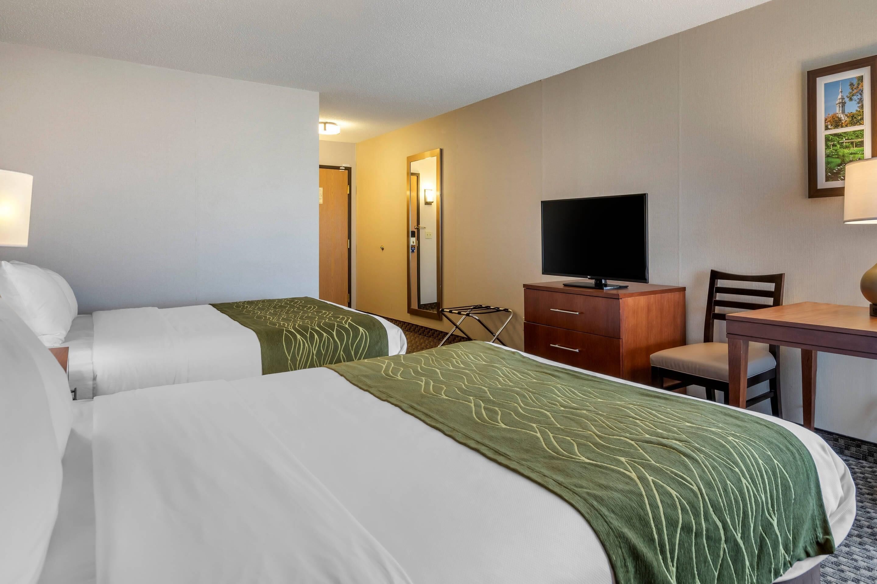 Ein Hotelzimmer mit zwei Betten, einem Fernseher, einem Schreibtisch und einem Sessel.