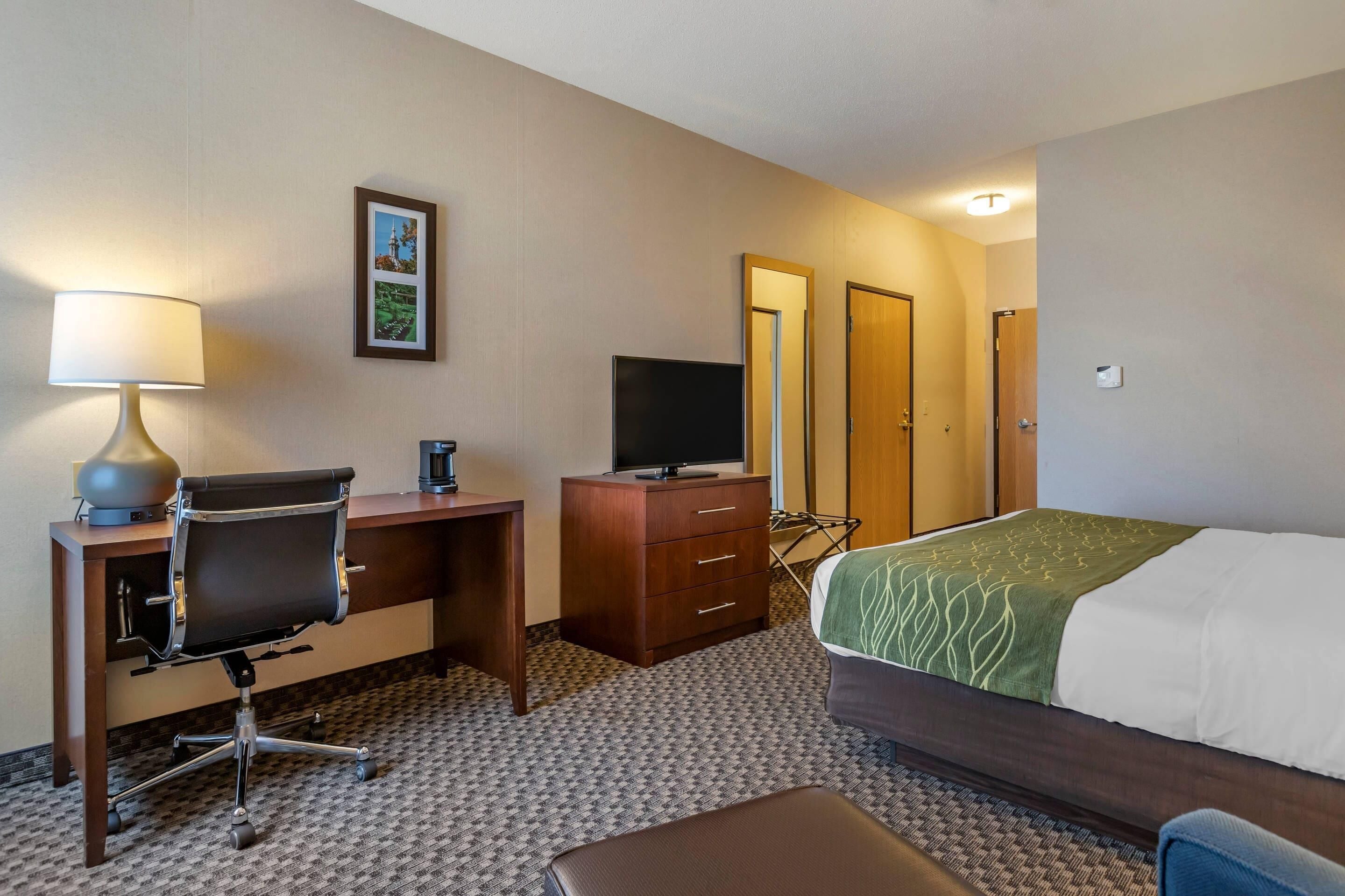 Habitación de hotel con escritorio, silla, televisor, armario, cama y una mesita.