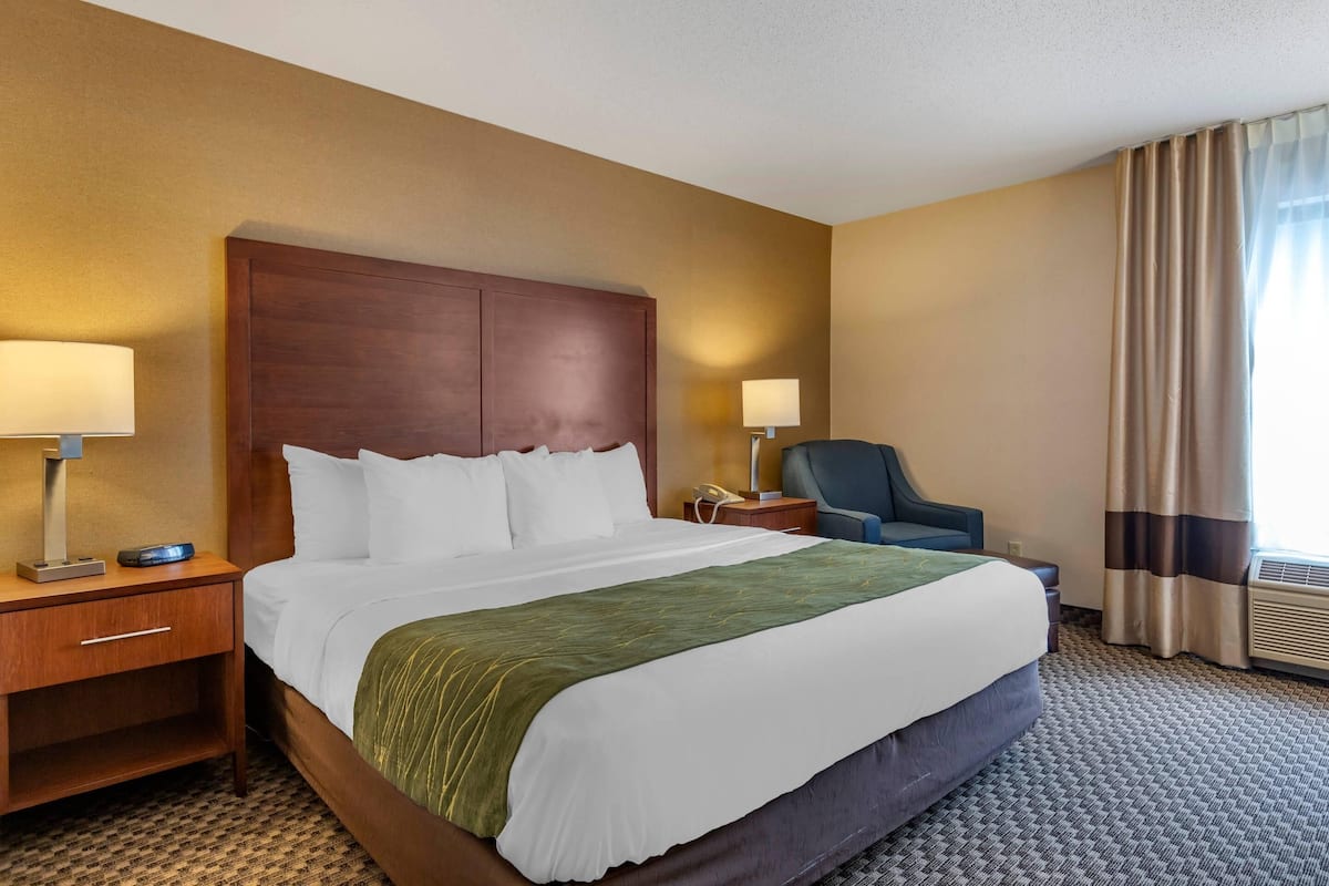 A hotel room with a large bed, bedside tables, a chair, and a window with curtains.