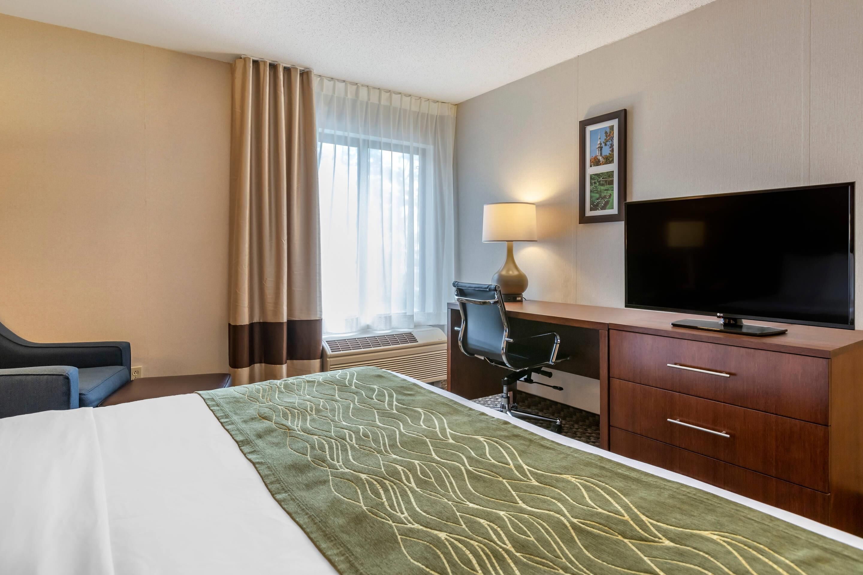 A hotel room with a bed, a desk with a TV, a chair, and a lamp.