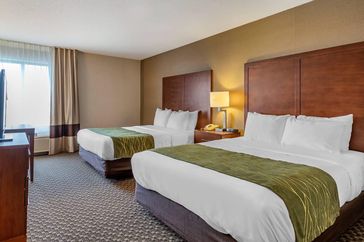 A hotel room with two beds, a desk, a lamp, and a telephone.