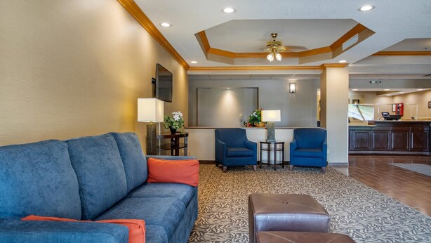 A modern living area with a sofa, ottoman, and chairs, a small table with a lamp, and a kitchen in the background. - Comfort Inn Charlotte (Charlotte)