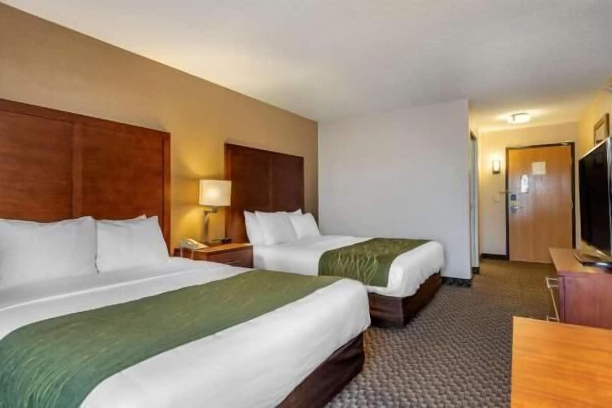 A hotel room with two beds, a desk, a lamp, and a television.