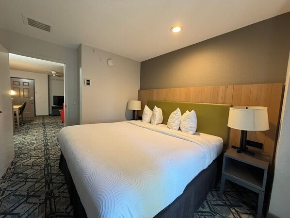 A hotel room with a large bed, two bedside lamps, a headboard, and a carpeted floor.