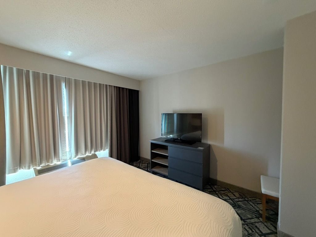 A hotel room with a large bed, a television on a stand, and a window with curtains.