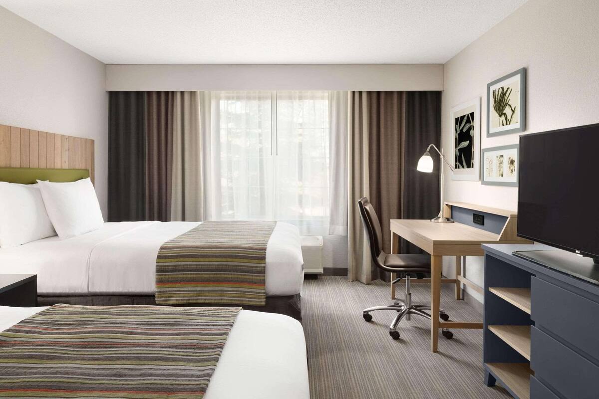A hotel room with two beds, a desk, a chair, a television, and artwork on the wall.