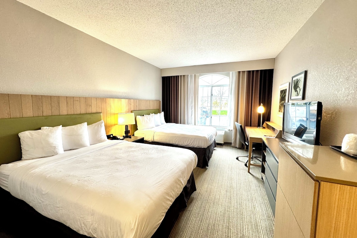 A hotel room with two beds, a desk, a TV, and a window with curtains.