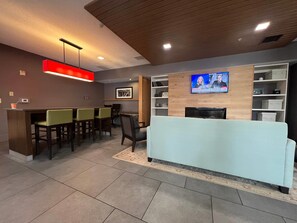 A modern lobby with a reception desk, seating area, and a television mounted on the wall.