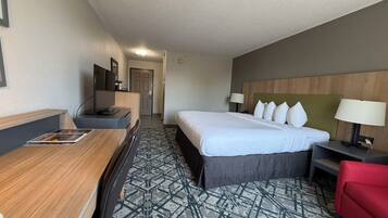 A hotel room with a bed, a desk, a chair, a TV, and a red couch.