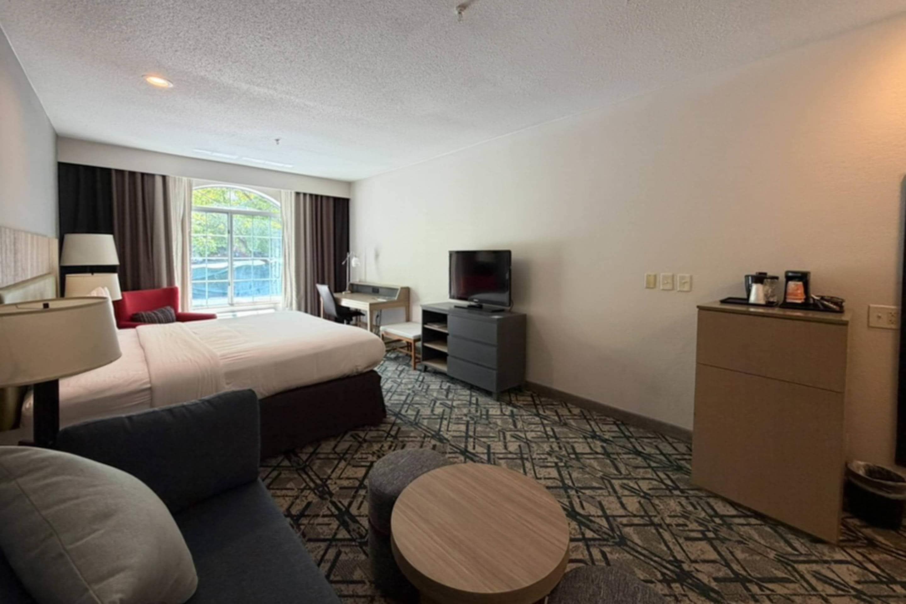 Una habitación de hotel con cama, escritorio, televisor, sofá y una pequeña mesa redonda.