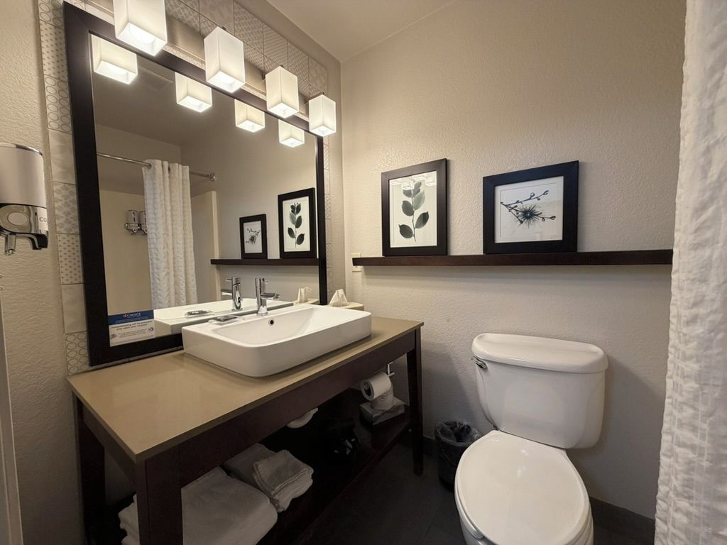 A bathroom with a white sink, mirror, and toilet. There are framed pictures on the wall and a towel rack.