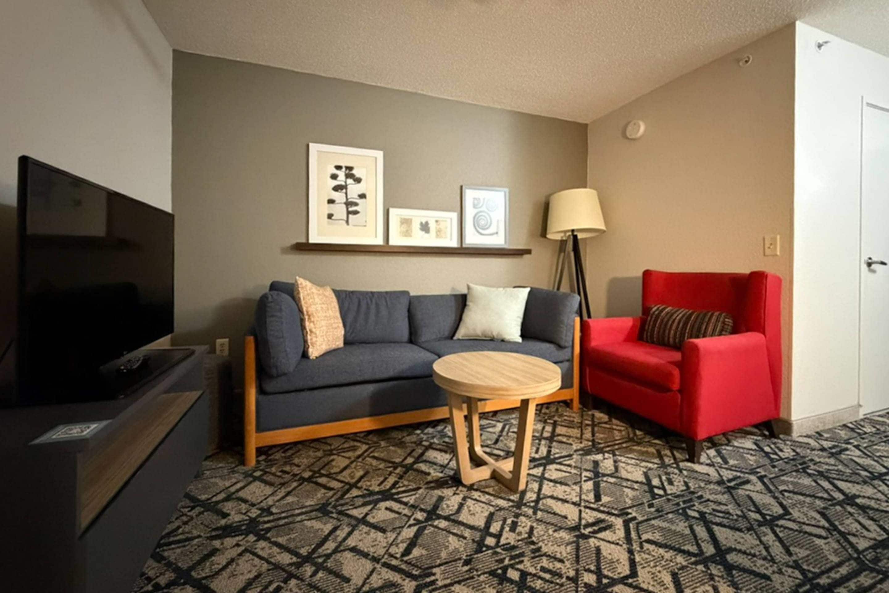 A living room with a sofa, a red armchair, a TV, and a patterned carpet.