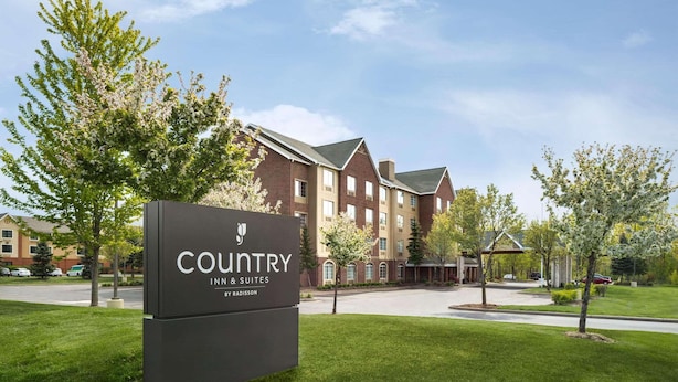 Une enseigne d’hôtel portant le nom « Country Inn & Suites by Radisson » devant un bâtiment en briques avec de nombreuses fenêtres et un toit végétalisé.