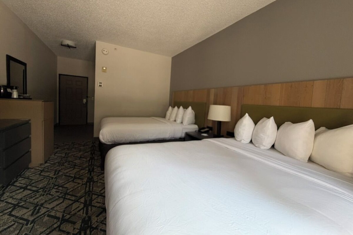 Una habitación de hotel con dos camas, un escritorio, una silla y un espejo.