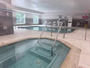 A swimming pool with steps and a lifeguard chair, surrounded by a tiled floor and a window with a view of trees. - Country Inn & Suites by Radisson, Novi, MI (Novi)