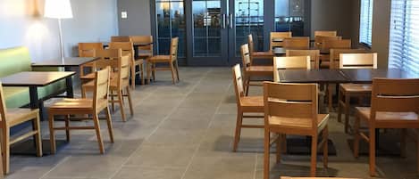 Un comedor espacioso con mesas y sillas de madera, piso de baldosas, y techo de listones con iluminación empotrada.