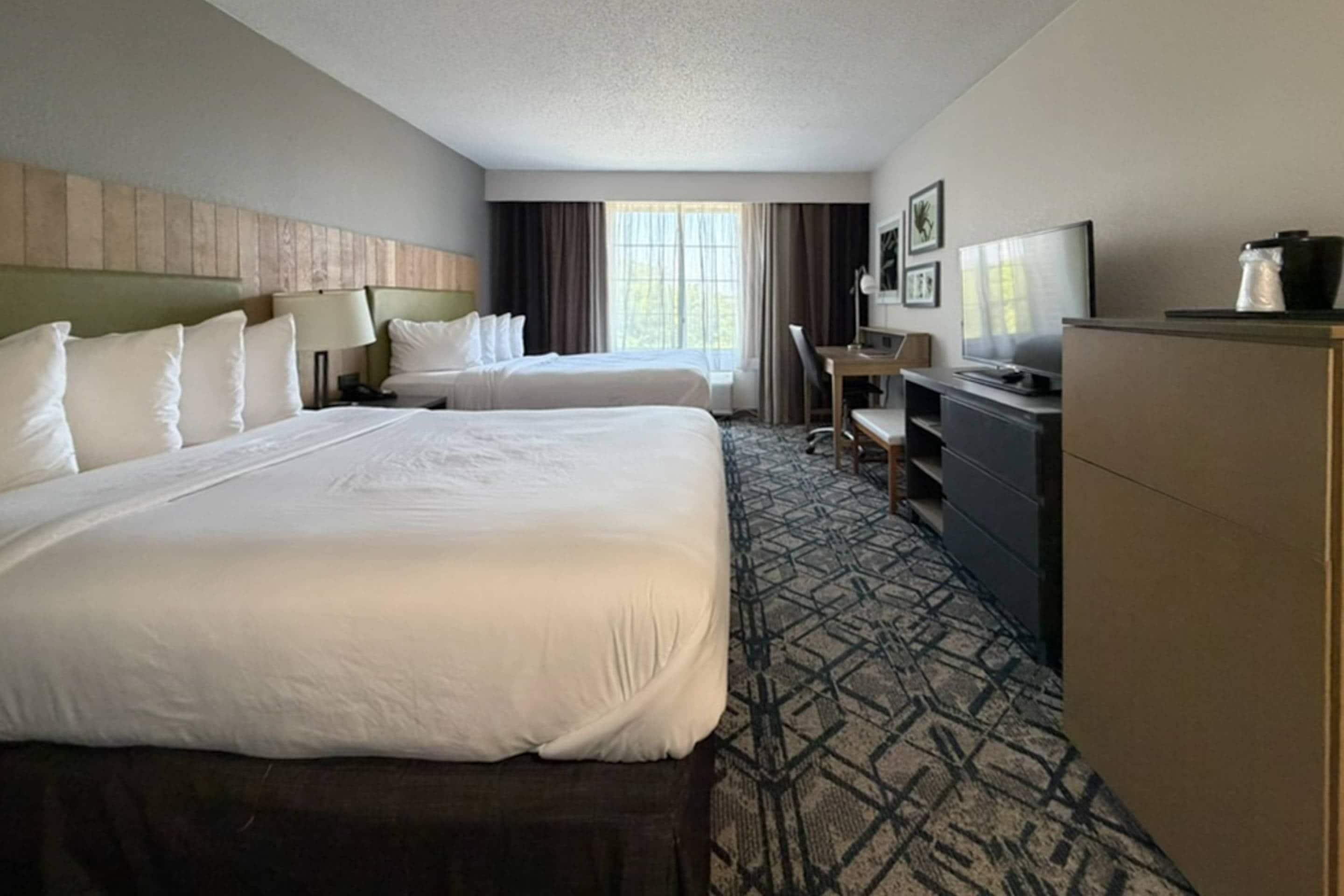A hotel room with two beds, a desk, a television, and a minibar.