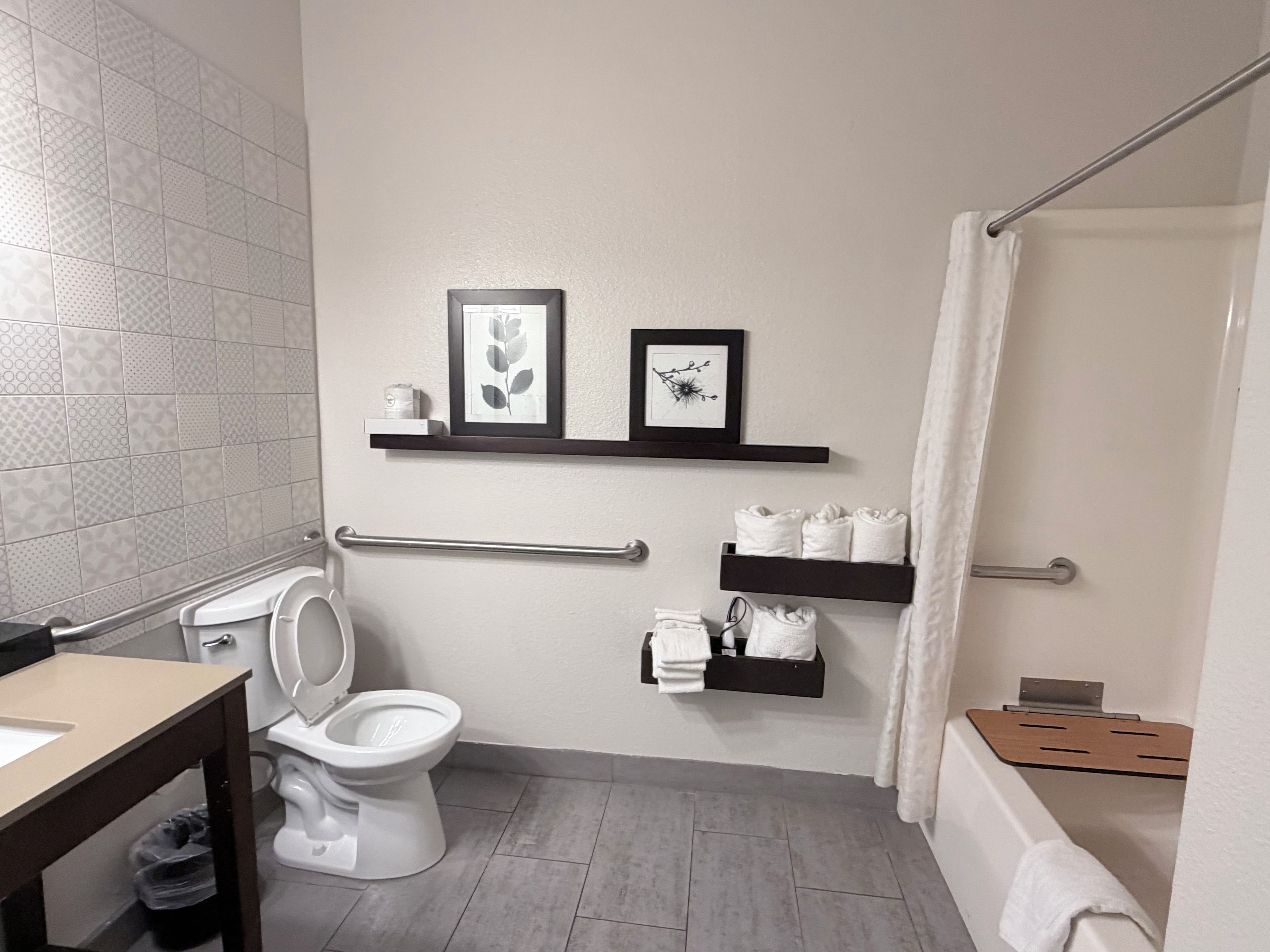 A modern bathroom with a toilet, a sink, and a shower area. There are framed pictures on the wall and a towel rack with towels.