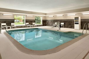 A swimming pool with a tiled deck, white lounge chairs, and a sauna area with a glass door.