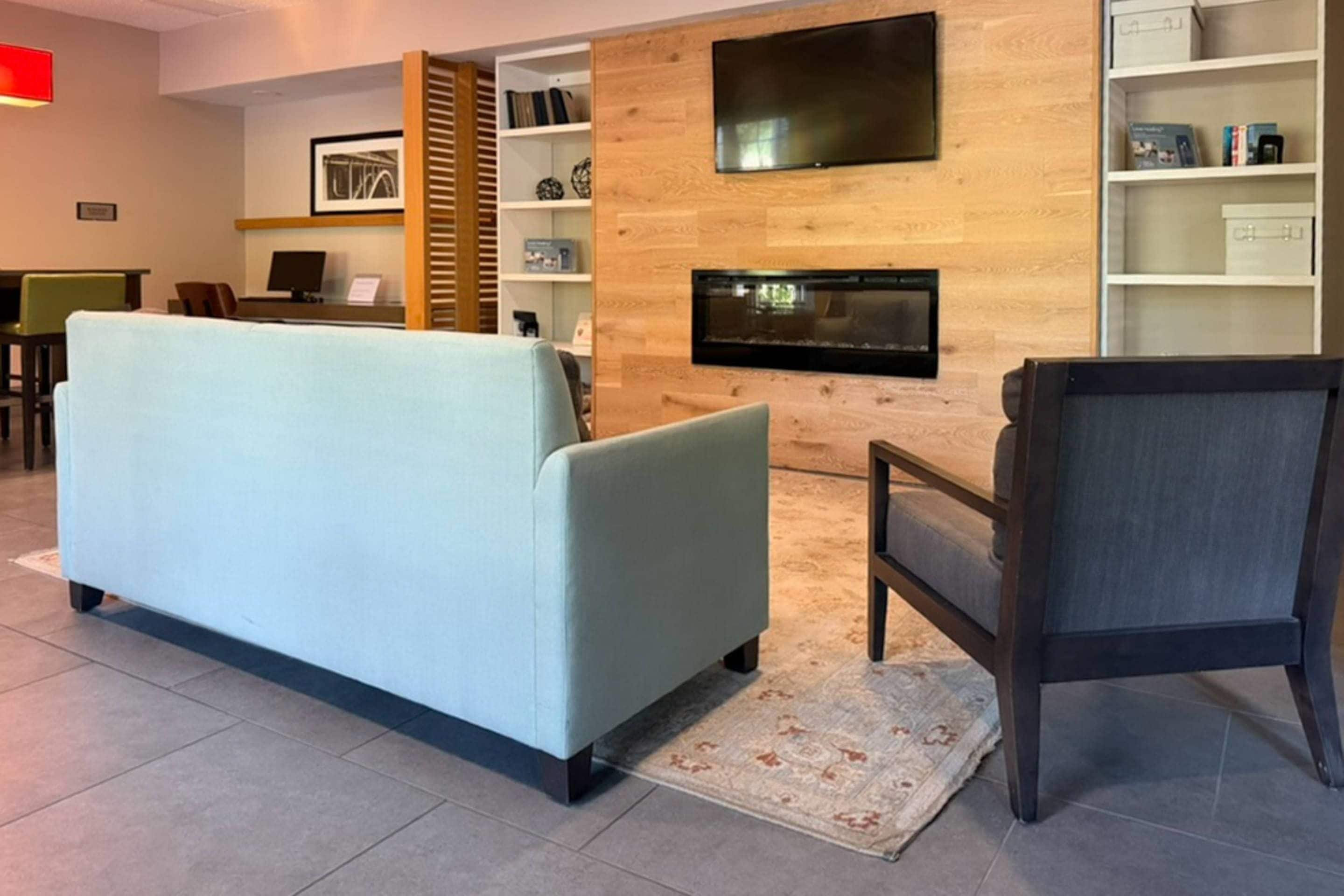 Uma sala de estar moderna com sofá, poltrona, TV de tela plana na parede e estante de livros.