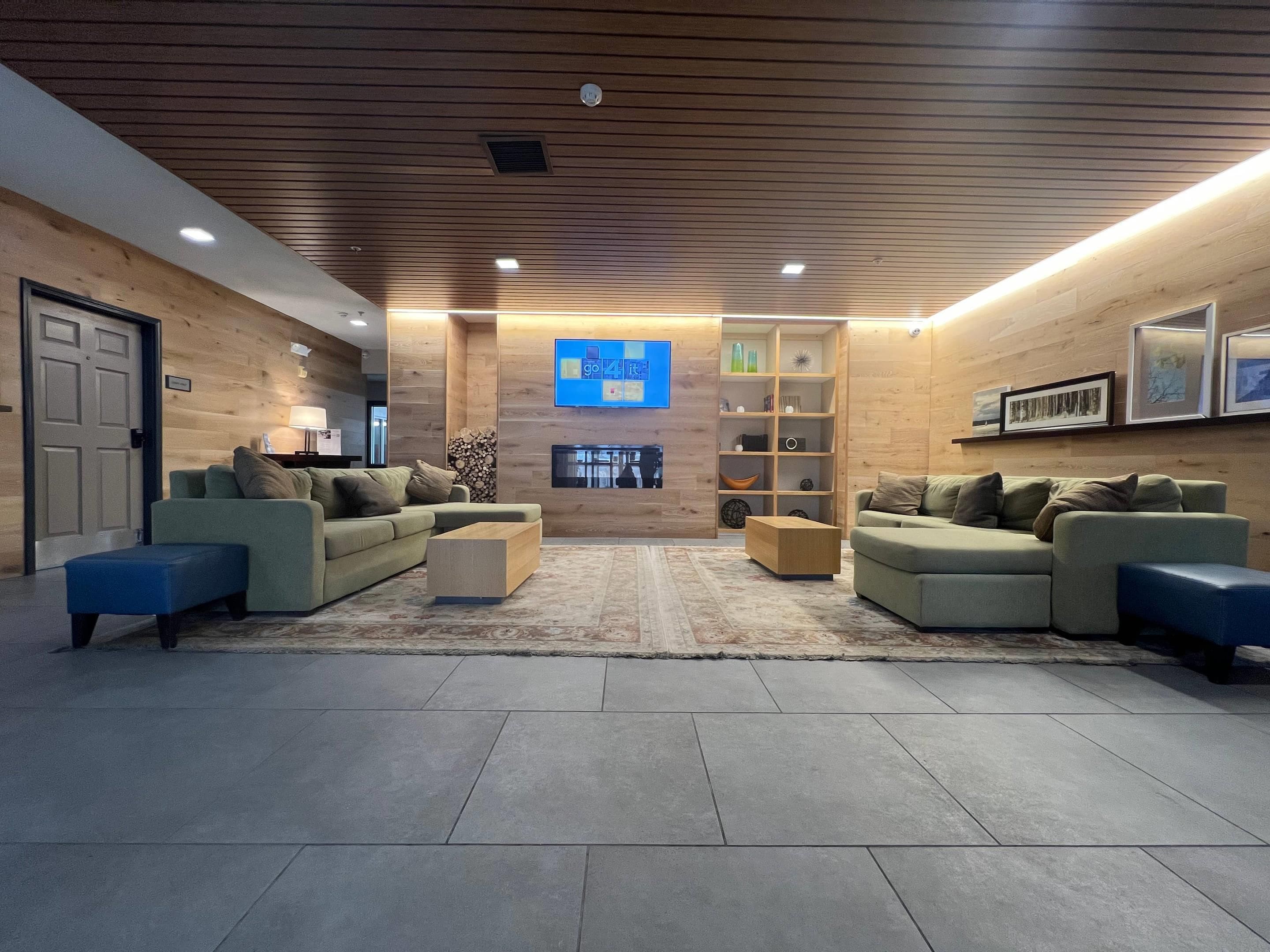 A modern lobby with sofas, a coffee table, a fireplace, and a digital screen.