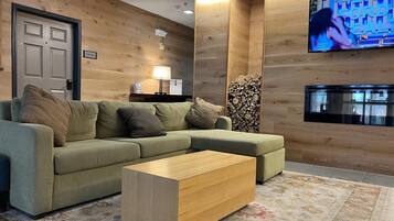 A modern living room with a sofa, a coffee table, a TV mounted on the wall, and a stack of firewood.