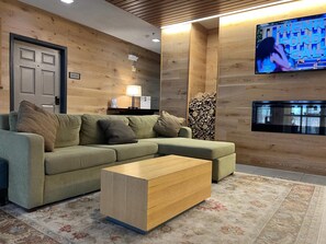 A modern living room with a sofa, a coffee table, a TV mounted on the wall, and a stack of firewood.