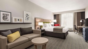 Une chambre d’hôtel avec un lit, un canapé, une petite table, un bureau et un téléviseur.