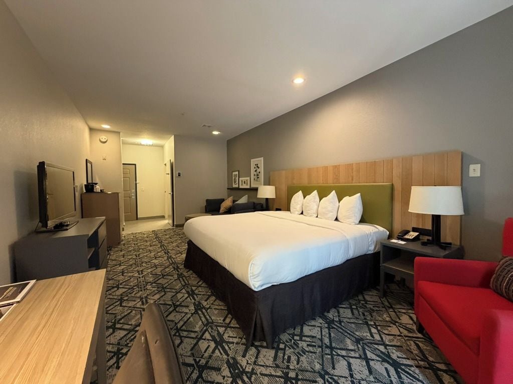 A hotel room with a large bed, a desk, a red armchair, and a television.